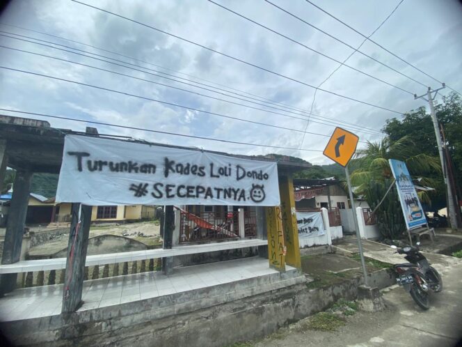 
					Spanduk membentang bertuliskan ‘Turunkan Kades Loli Dondo Secepatnya’ terpanpang di depan Kantor Desa. FOTO: netiz.id (Akib).